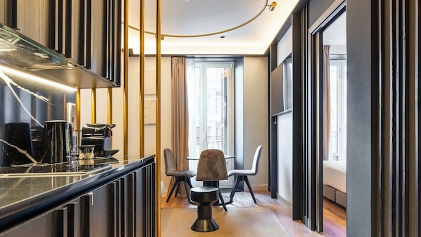 A modern hotel room with a sleek black bar, a large window with curtains, and a minimalist seating area.