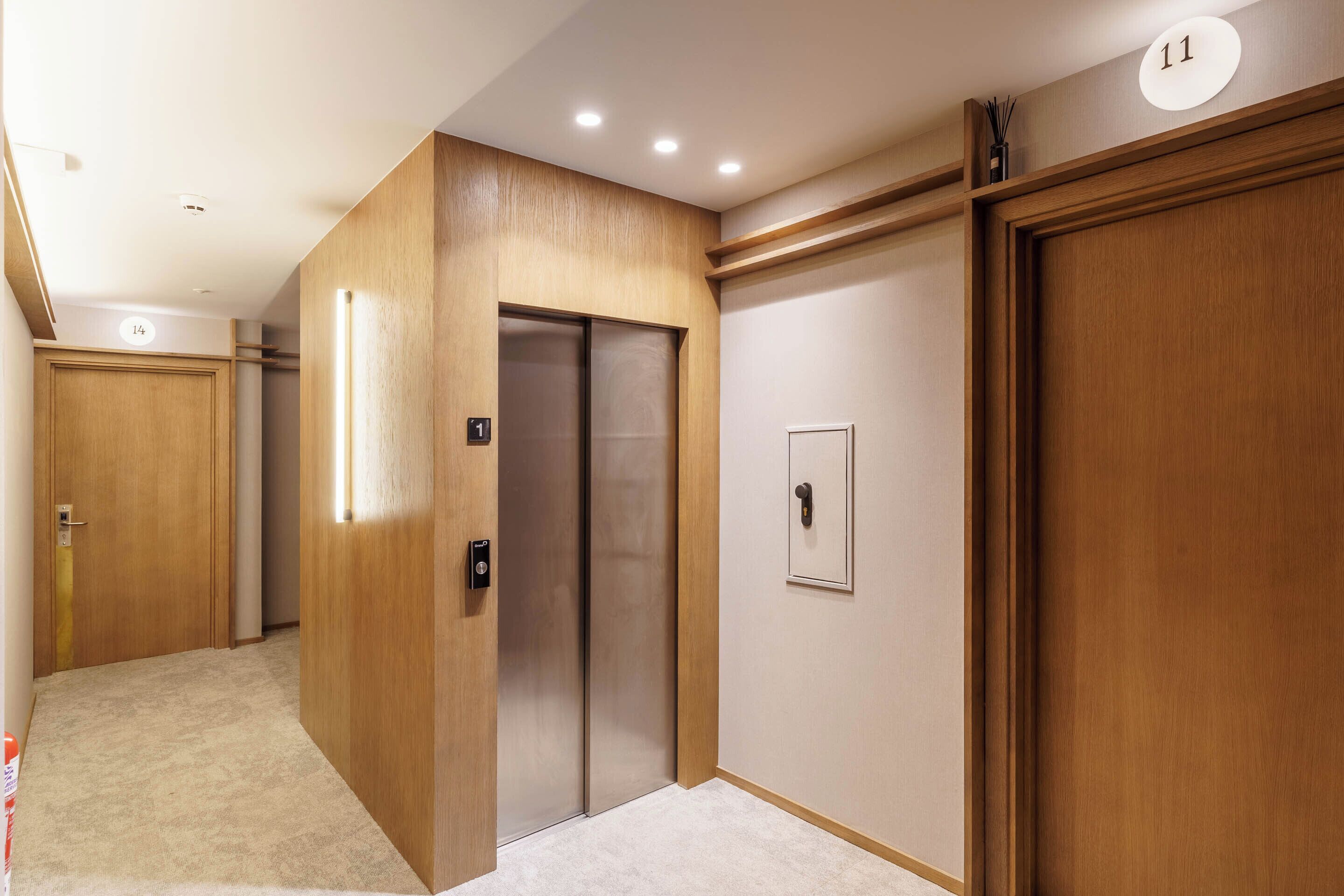 A hallway with wooden doors, an elevator, and a number sign indicating room 11.