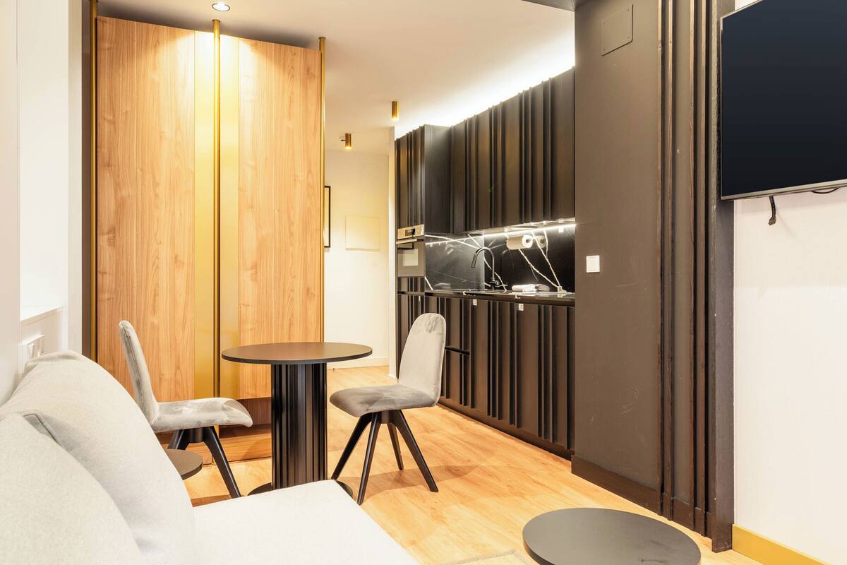 Une cuisine compacte dotée d’appareils électroménagers modernes, un coin repas avec une table ronde et deux chaises, et une cloison en bois.