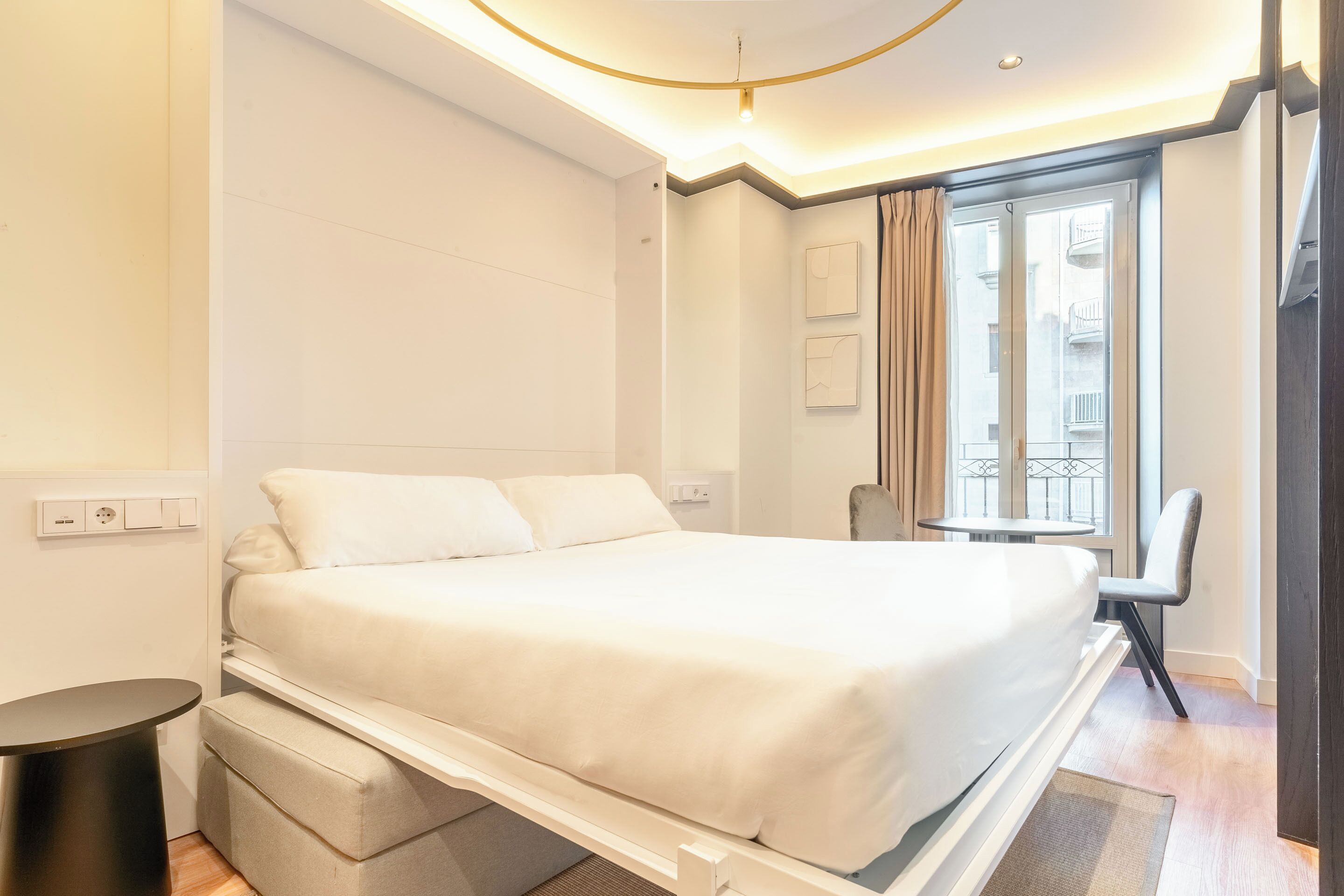 Una camera d'albergo moderna con un letto grande, un tavolino, una sedia e una finestra con tende.