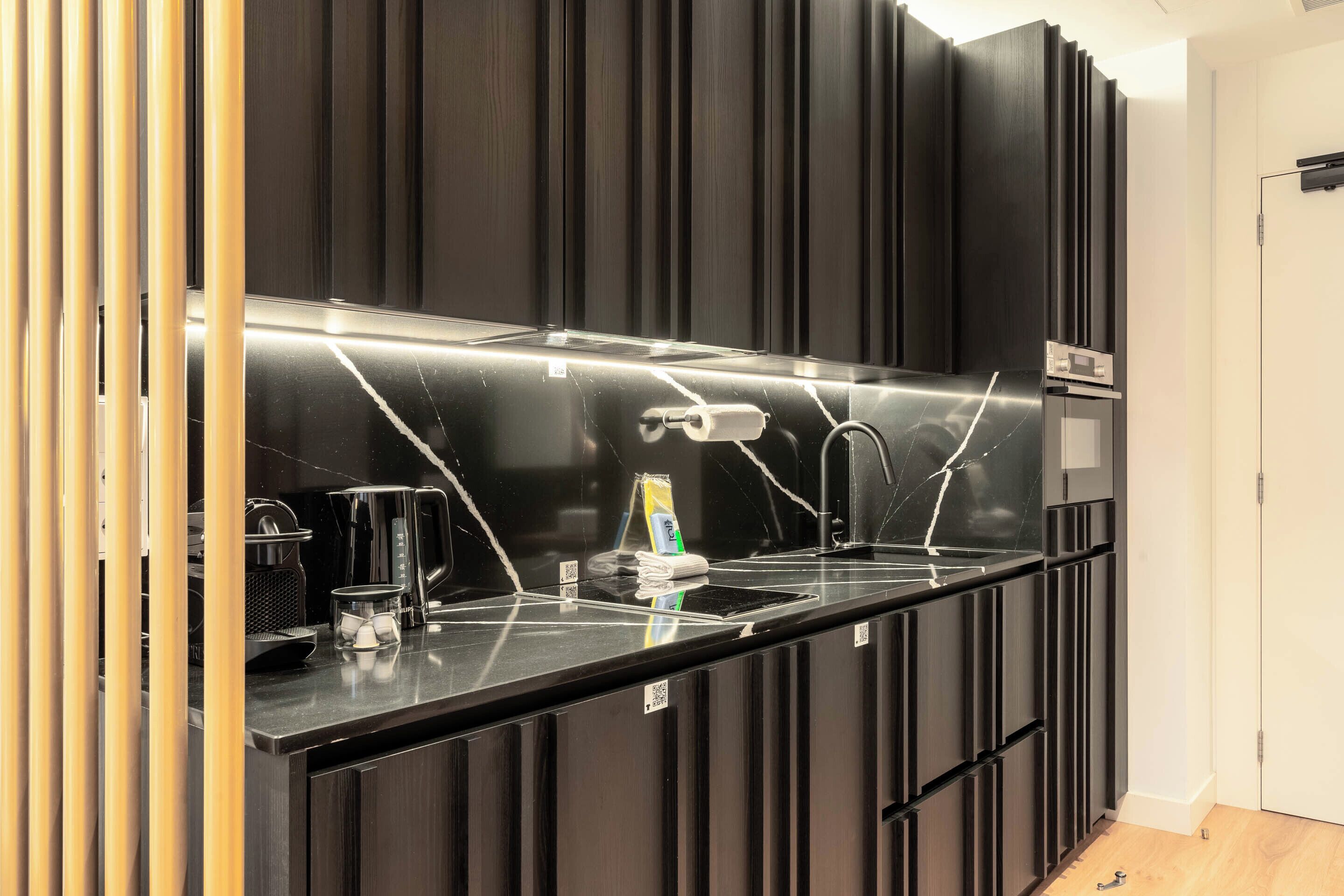A modern kitchen with a black countertop, stainless steel appliances, and a dark wooden panel wall.