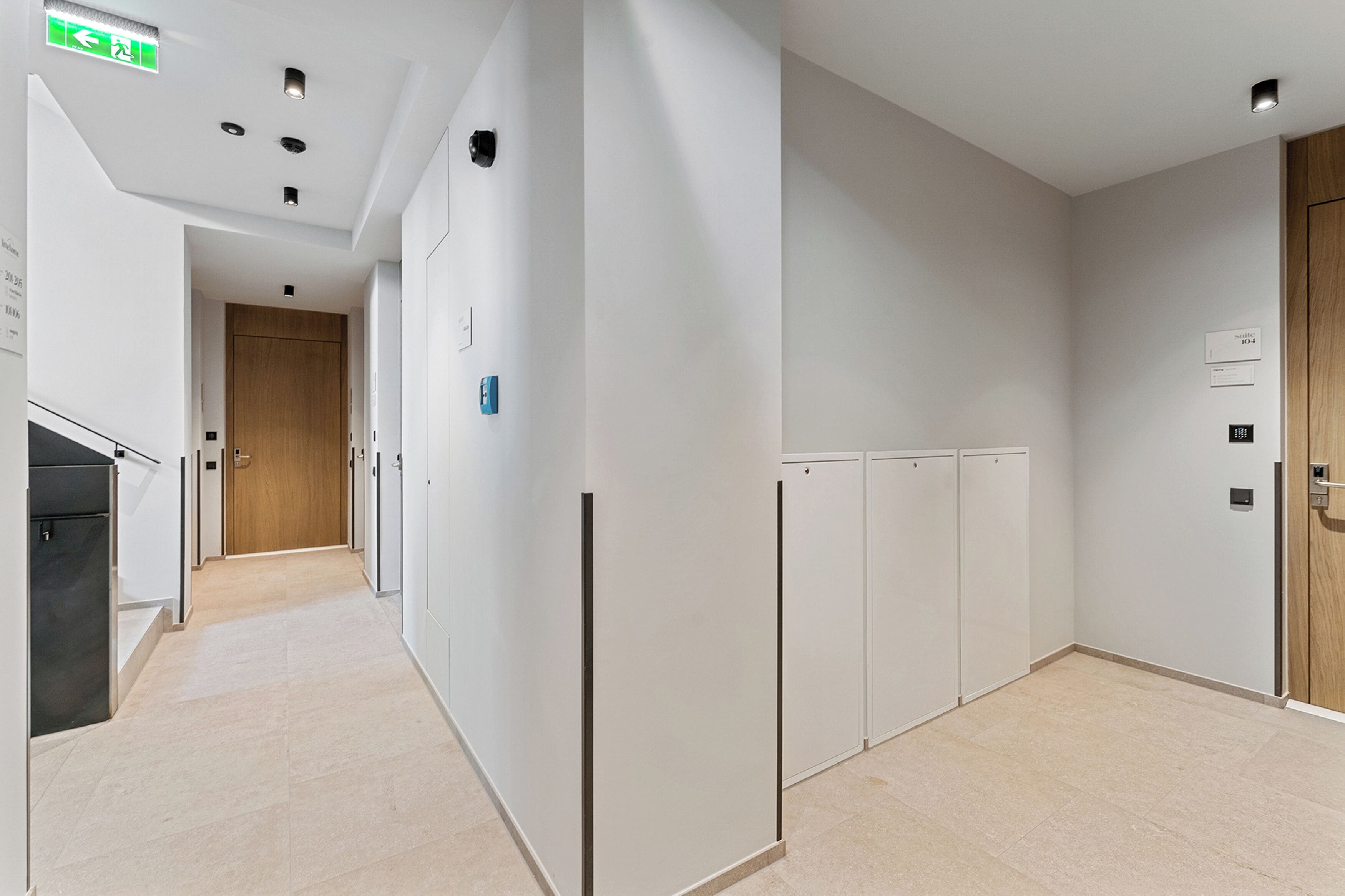 A modern hallway with a wooden door at the end, white walls, and a tiled floor.