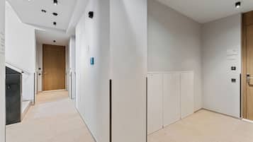 A modern hallway with a wooden door at the end, white walls, and a tiled floor.