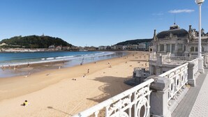 A beach with a white ornate railing, a clear blue sky, and buildings in the background.