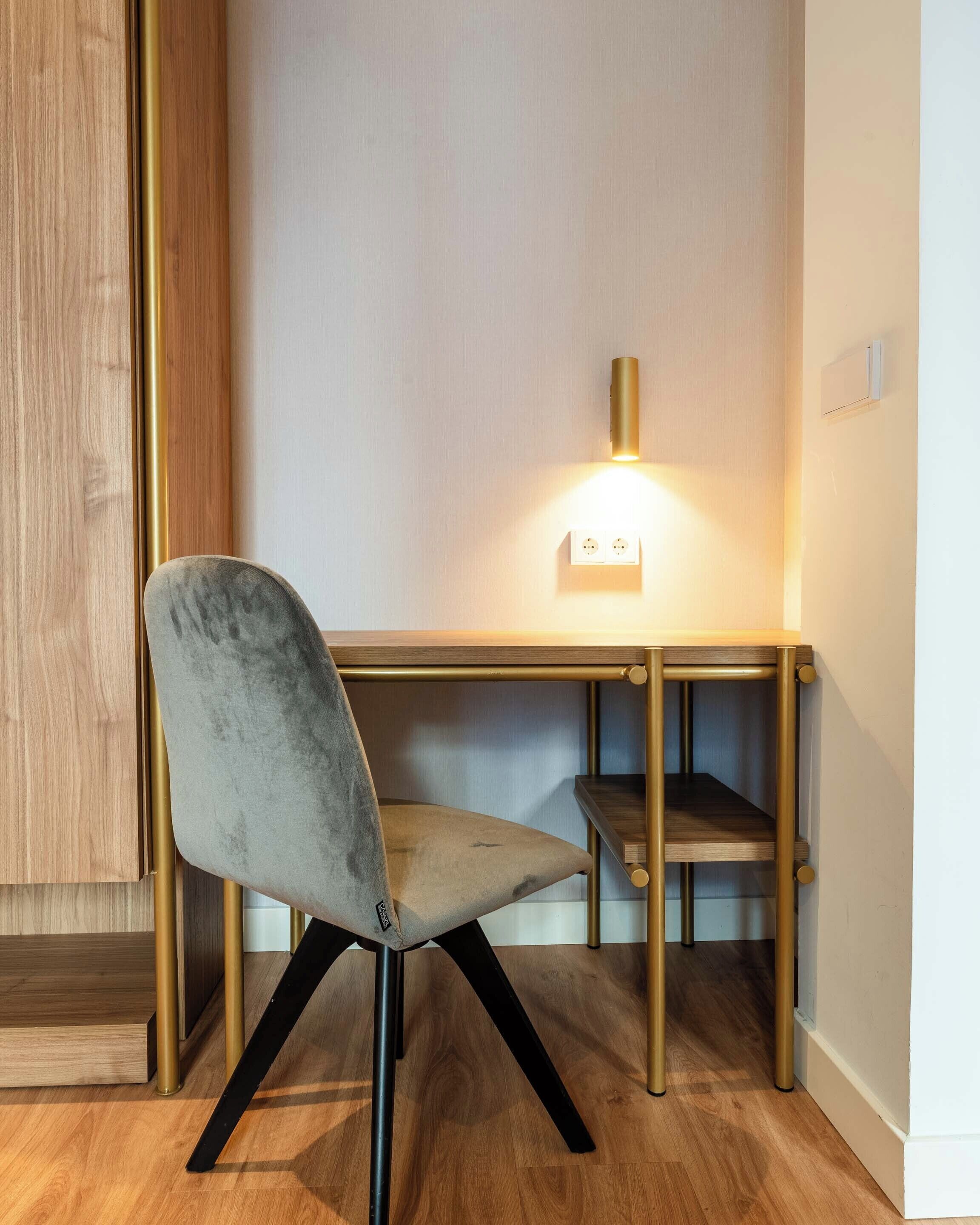 A modern desk with a chair, a wall-mounted light, and a power outlet.