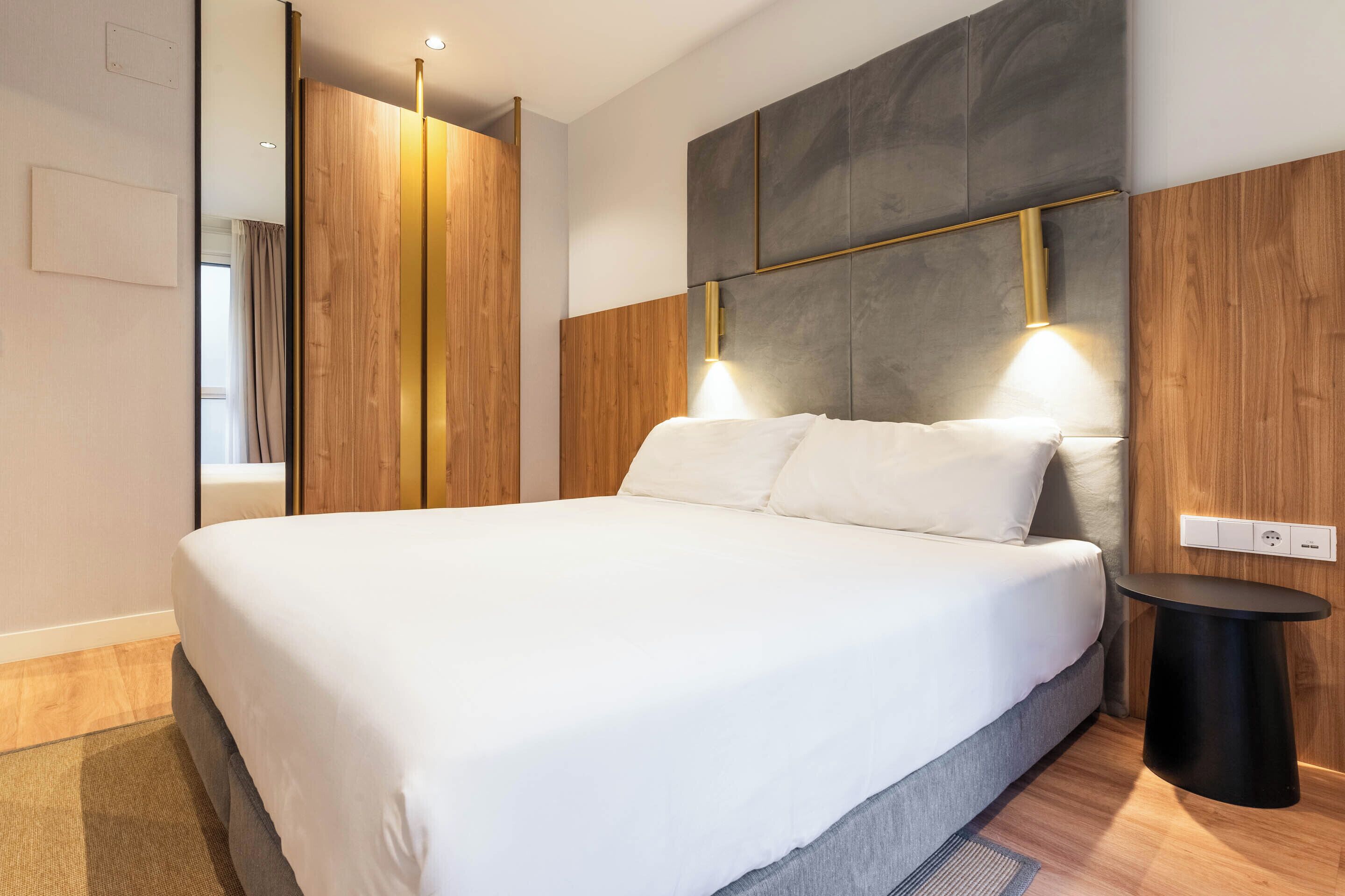 Un dormitorio moderno con una cama grande, paneles de madera en las paredes y una mesita redonda cerca de la cama.