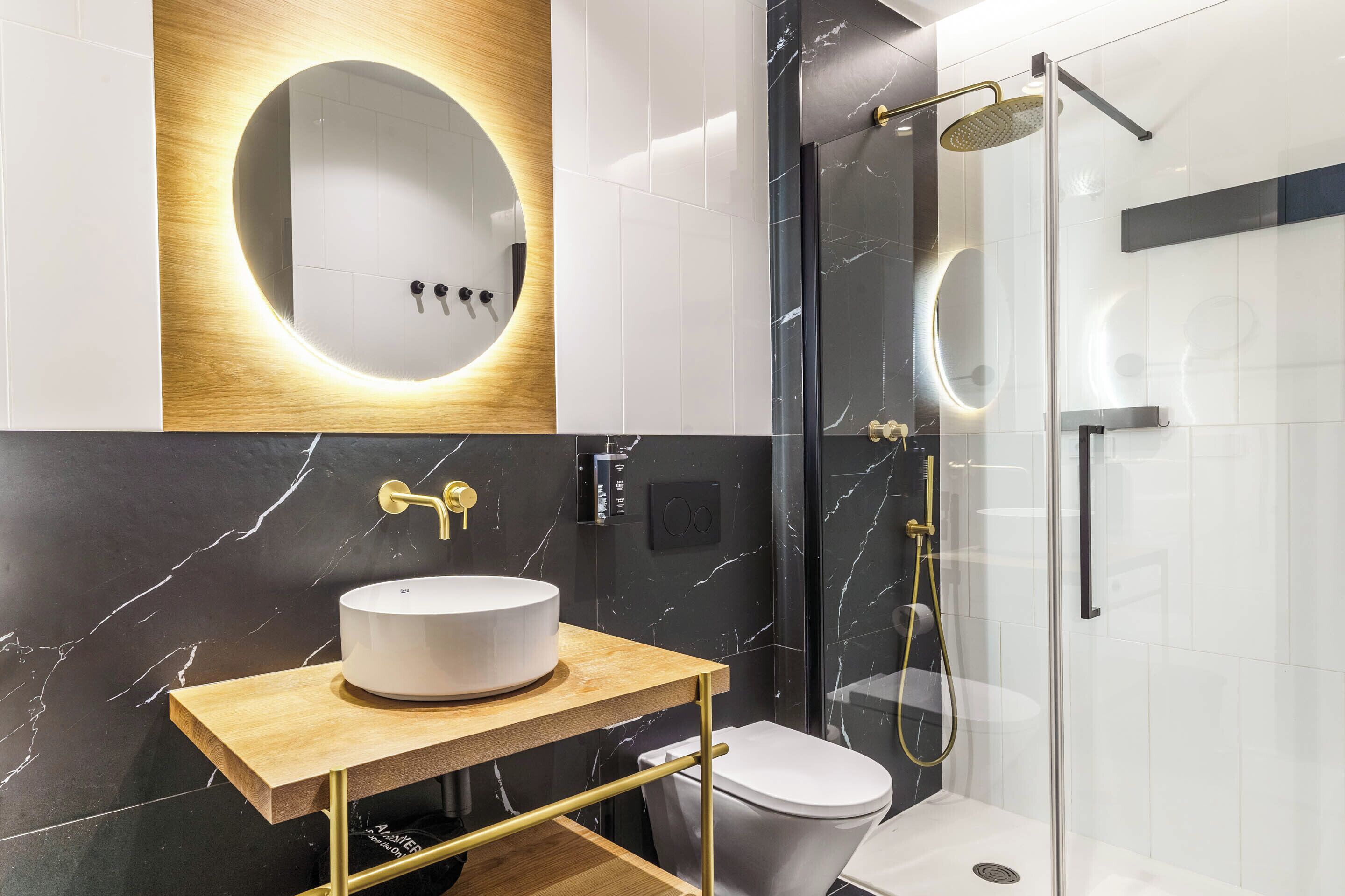 A modern bathroom with a round mirror, a white sink, and a glass-enclosed shower.