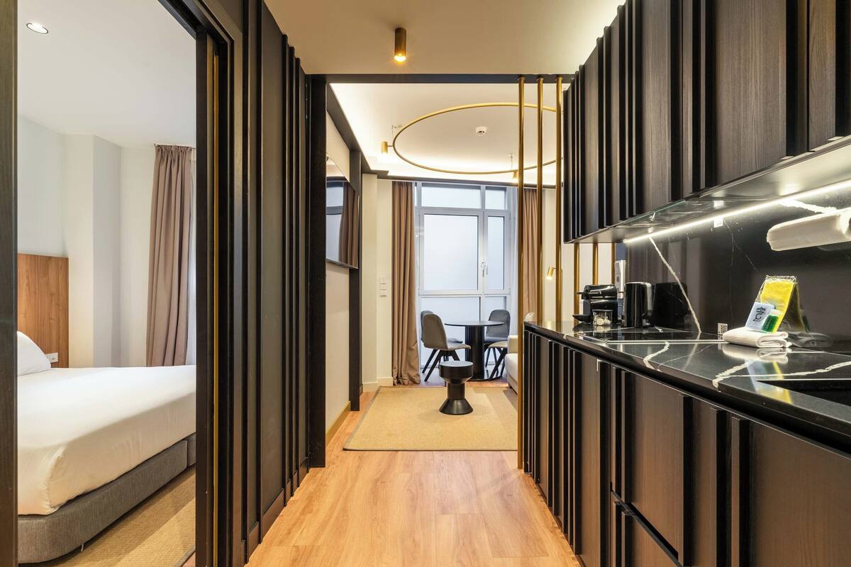 Une chambre d’hôtel comprenant un lit, un petit bureau avec une chaise, une machine à café et donnant sur la salle à manger.