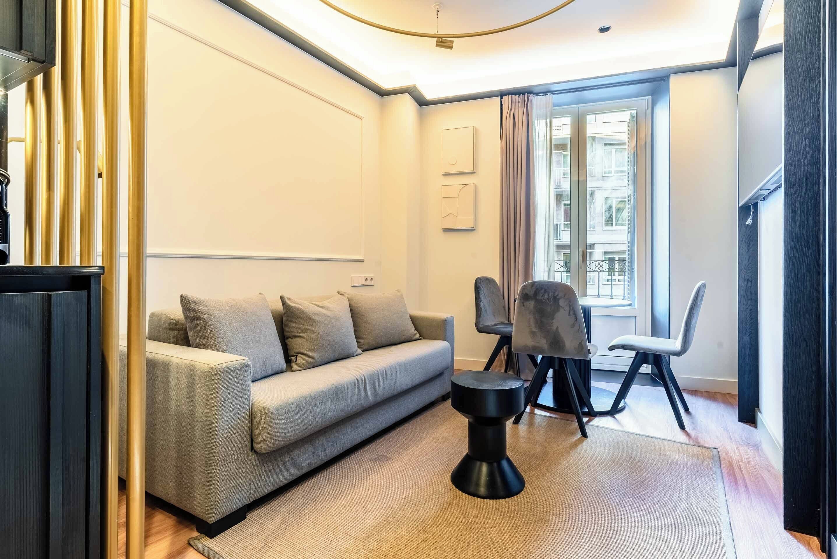 Un salon moderne avec un canapé, des fauteuils, une table basse et une grande fenêtre agrémentée de rideaux.