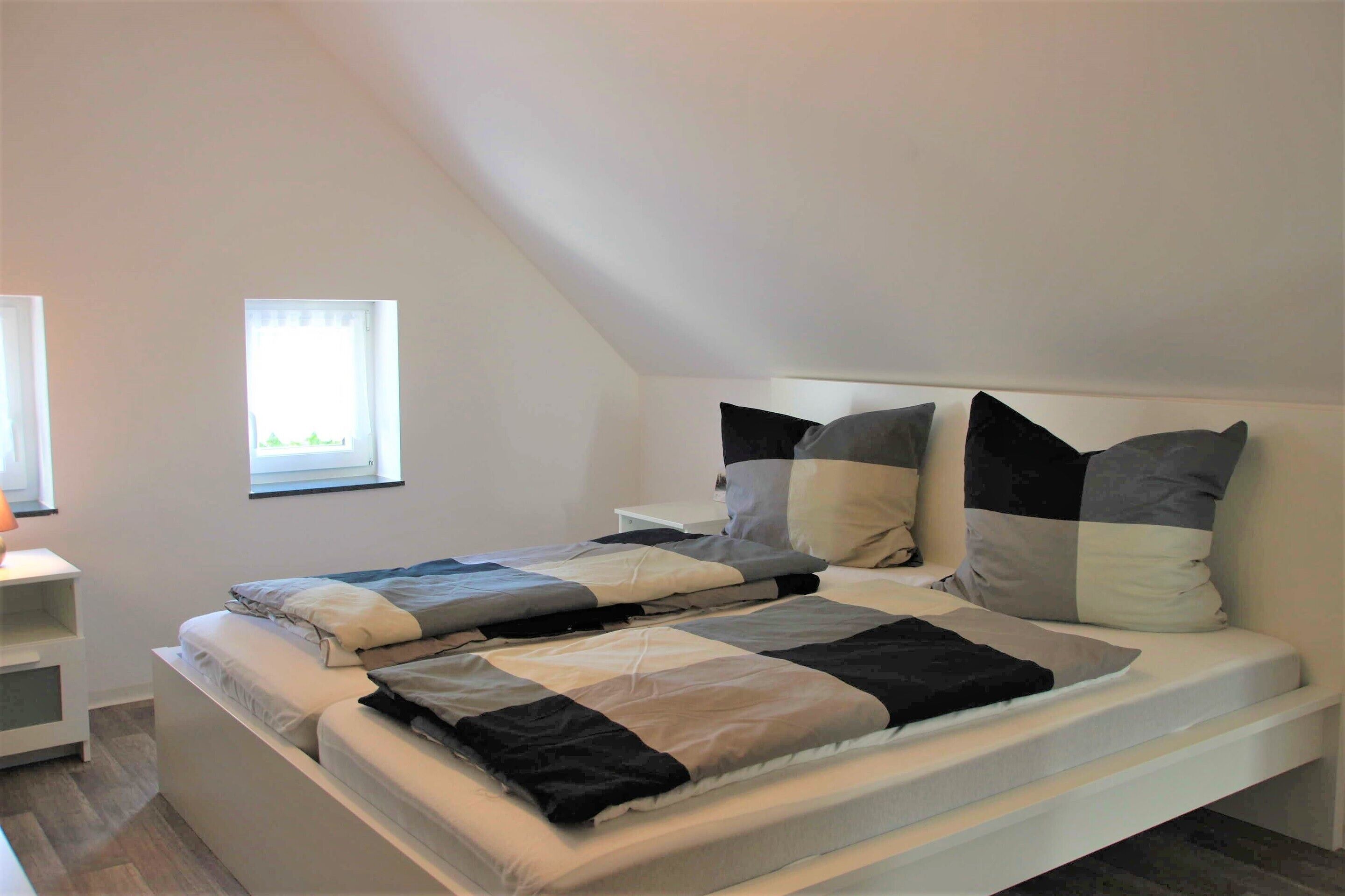Un dormitorio con cama, almohadas, mesita de noche y ventana.