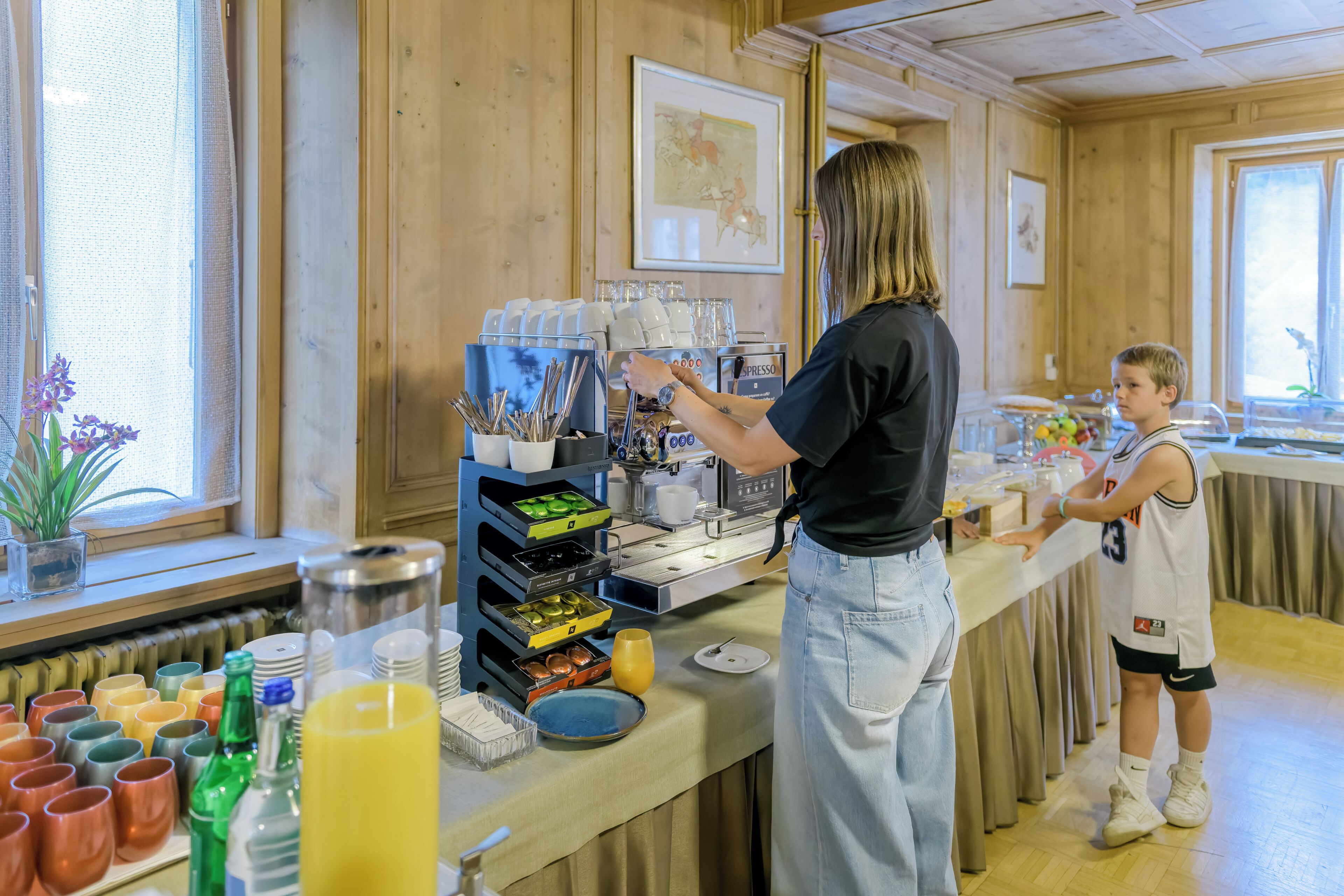 Een ontbijtbuffet met koffieautomaten, een kind en een vrouw.