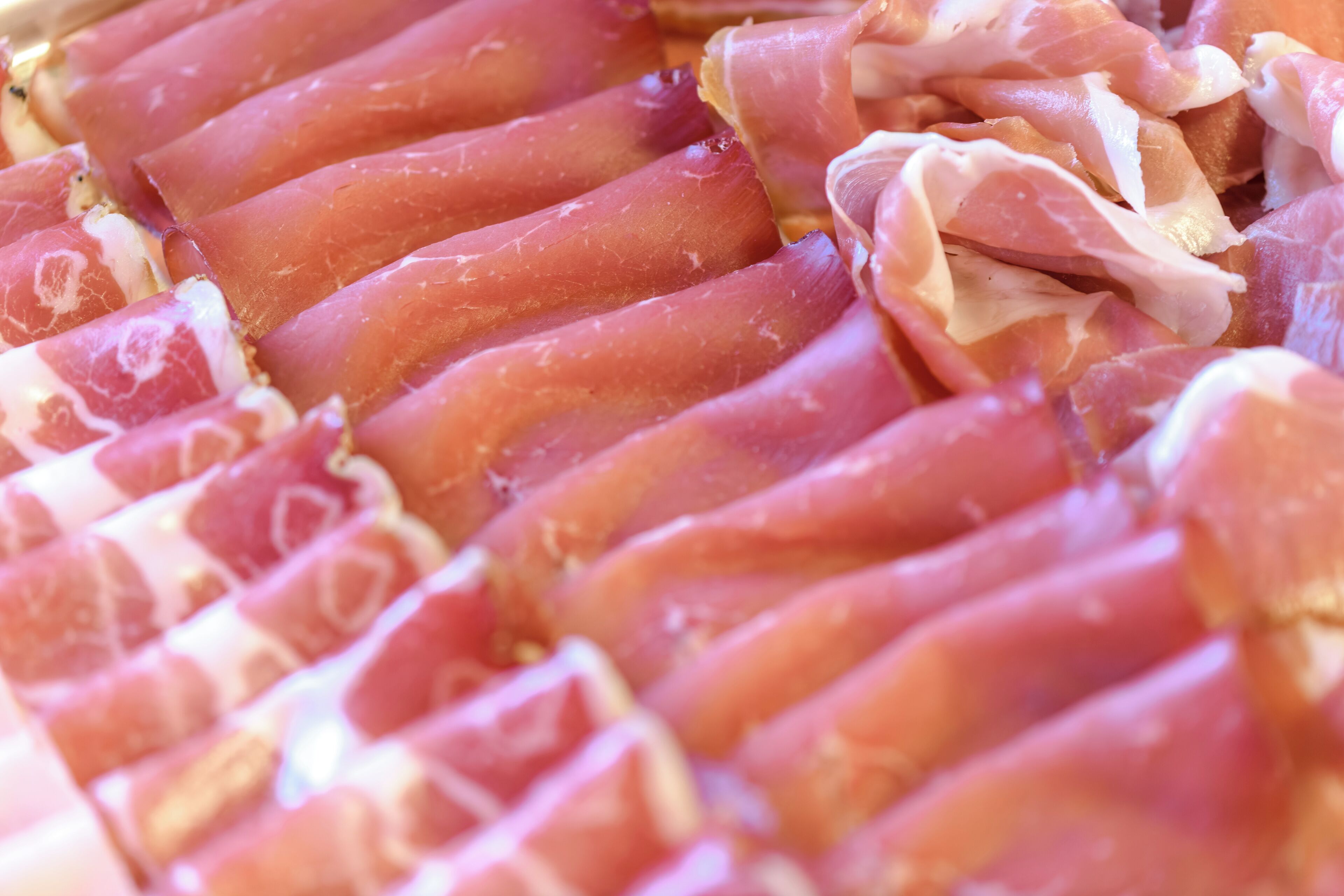A close-up of thinly sliced cured meat, likely prosciutto, arranged in a neat pattern.