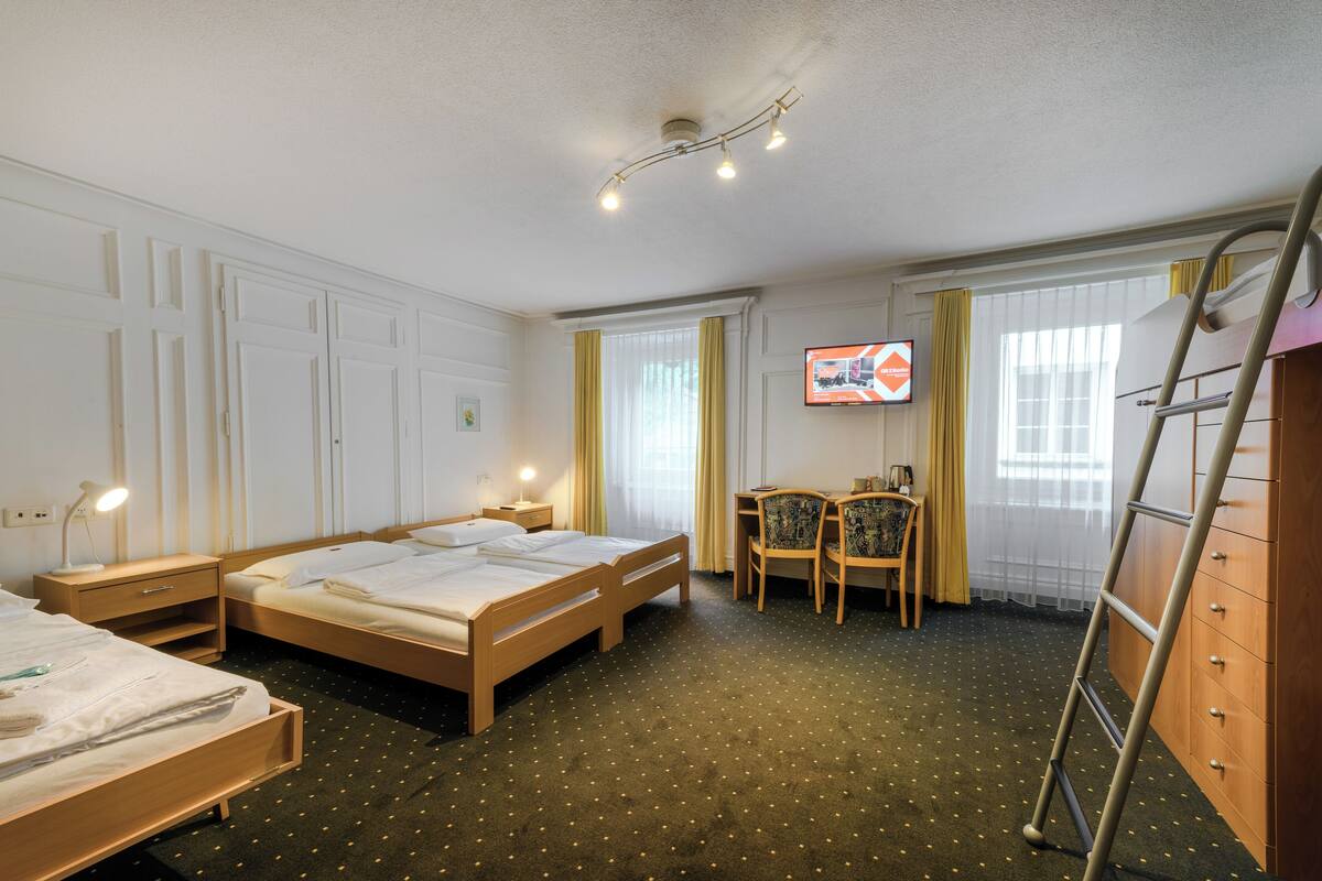 Ein Hotelzimmer mit zwei Betten, einem Schreibtisch mit Stuhl, einem Fernseher und einer Leiter.