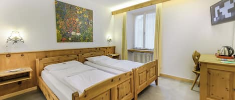 Una cama doble de madera con ropa blanca, una mesita de noche de madera, un aparador de madera, un cuadro colgado en la pared, una ventana con cortinas y un espejo.