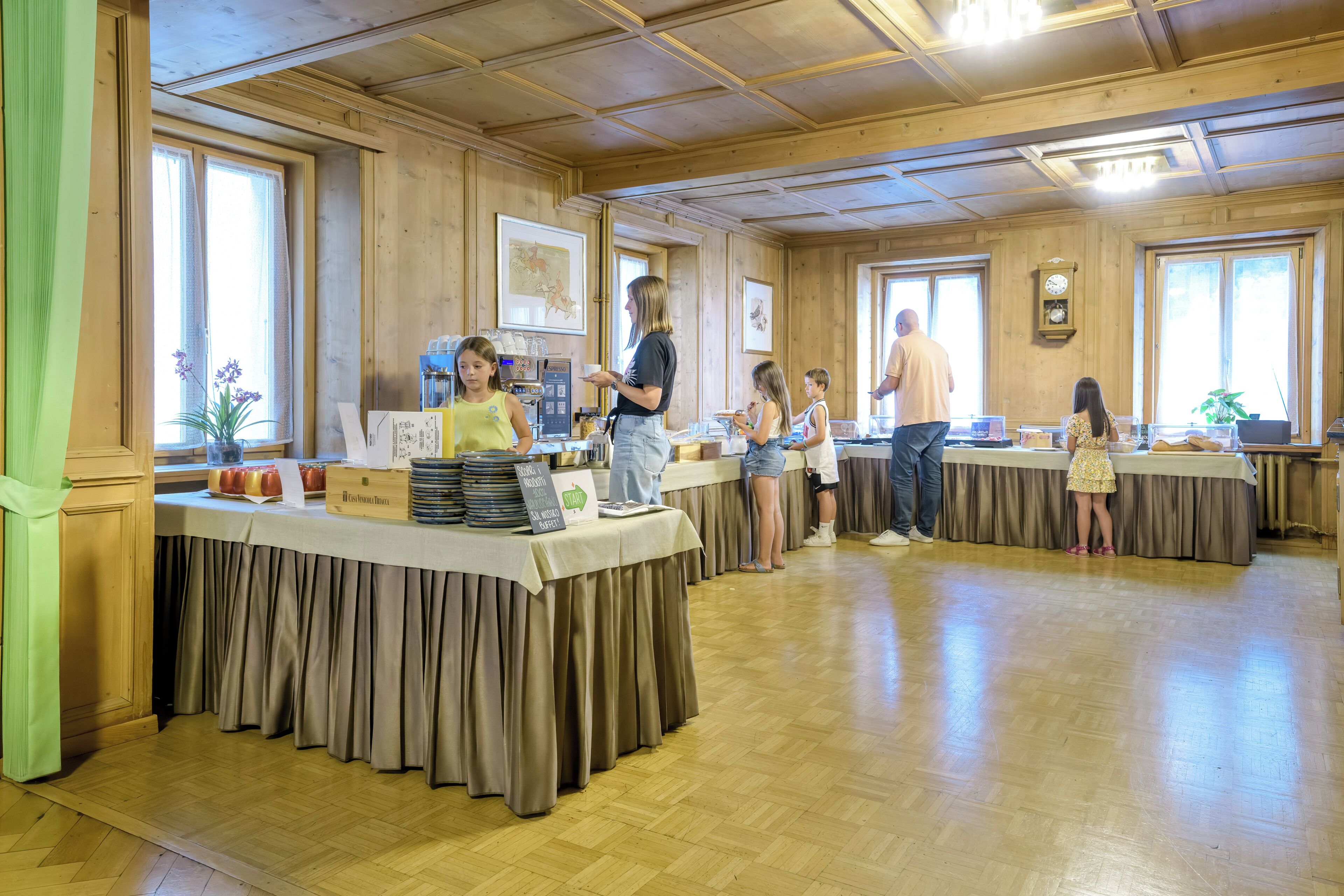 A room with wooden walls and ceiling, a long table with a tablecloth, and a clock on the wall.