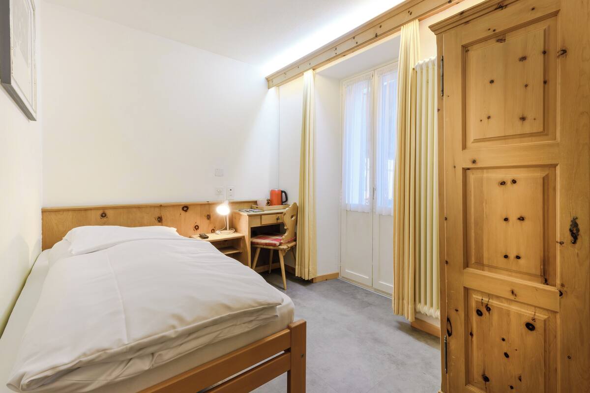 Ein Schlafzimmer mit einem Bett, einem Schreibtisch mit Stuhl, einem Heizkörper und einem Kleiderschrank.
