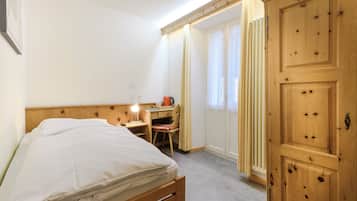 A bedroom with a bed, a desk with a chair, a radiator, and a wardrobe.