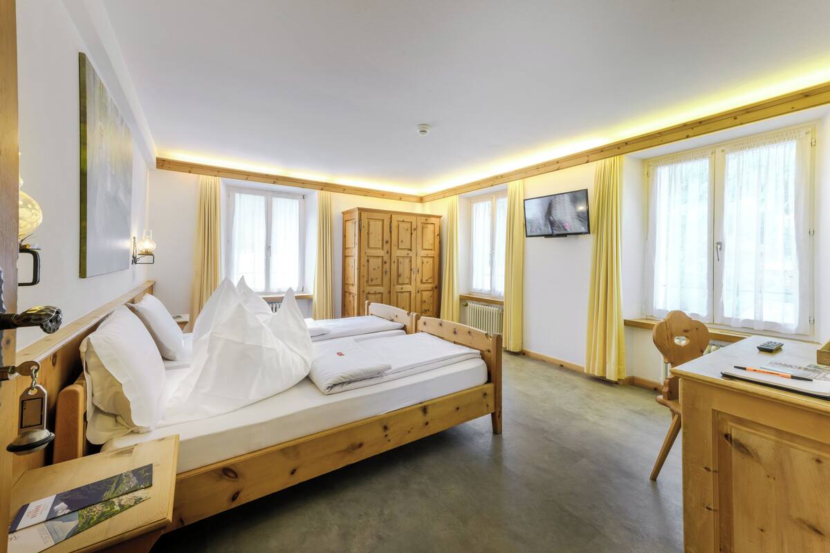 Ein Zimmer mit zwei Holzbetten, einem Schreibtisch mit Stuhl, einem Wandfernseher und einem Fenster mit Vorhängen.