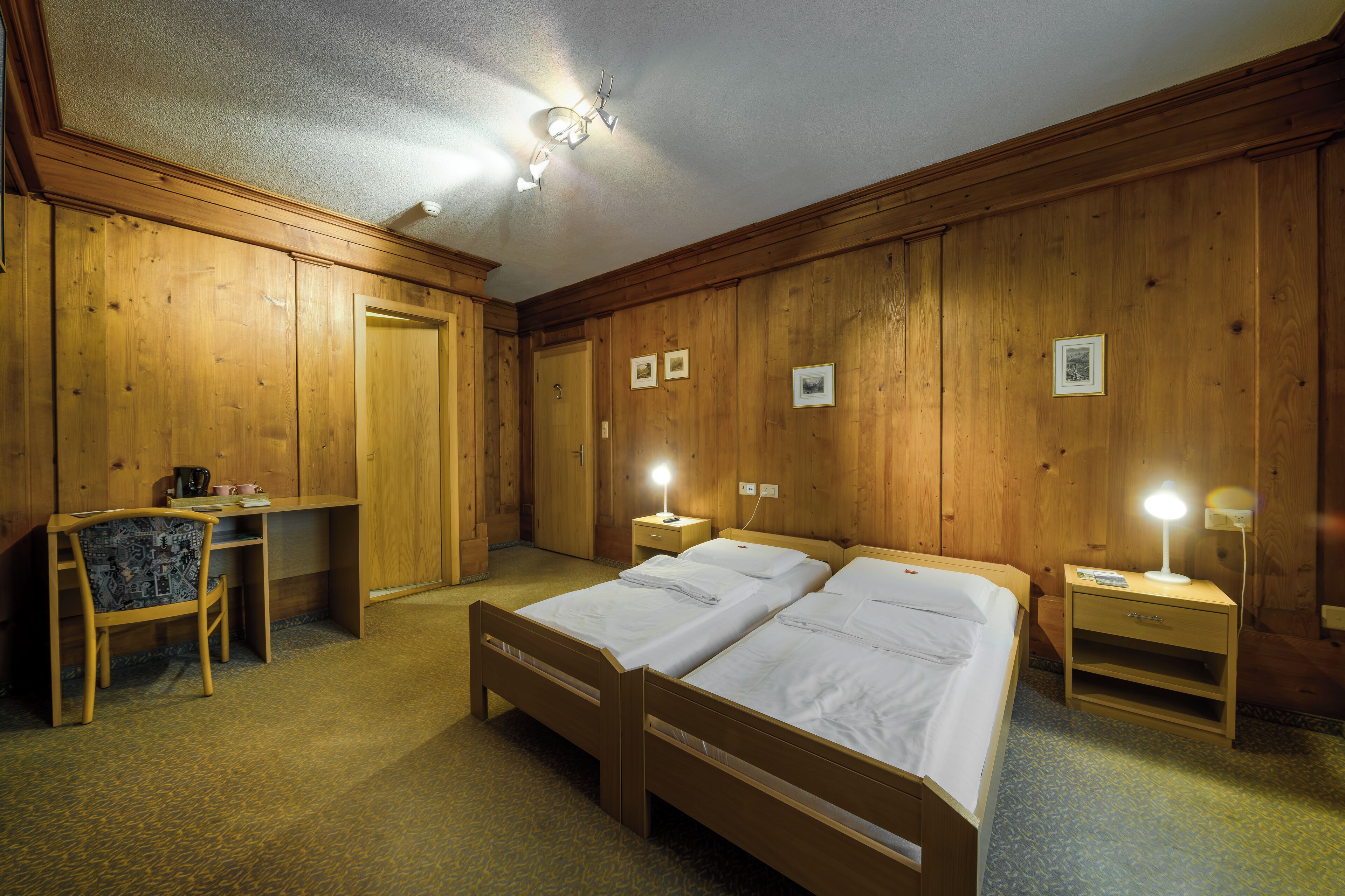 Ein Zimmer mit Holzwänden, zwei Betten, einem Schreibtisch und einem Stuhl.