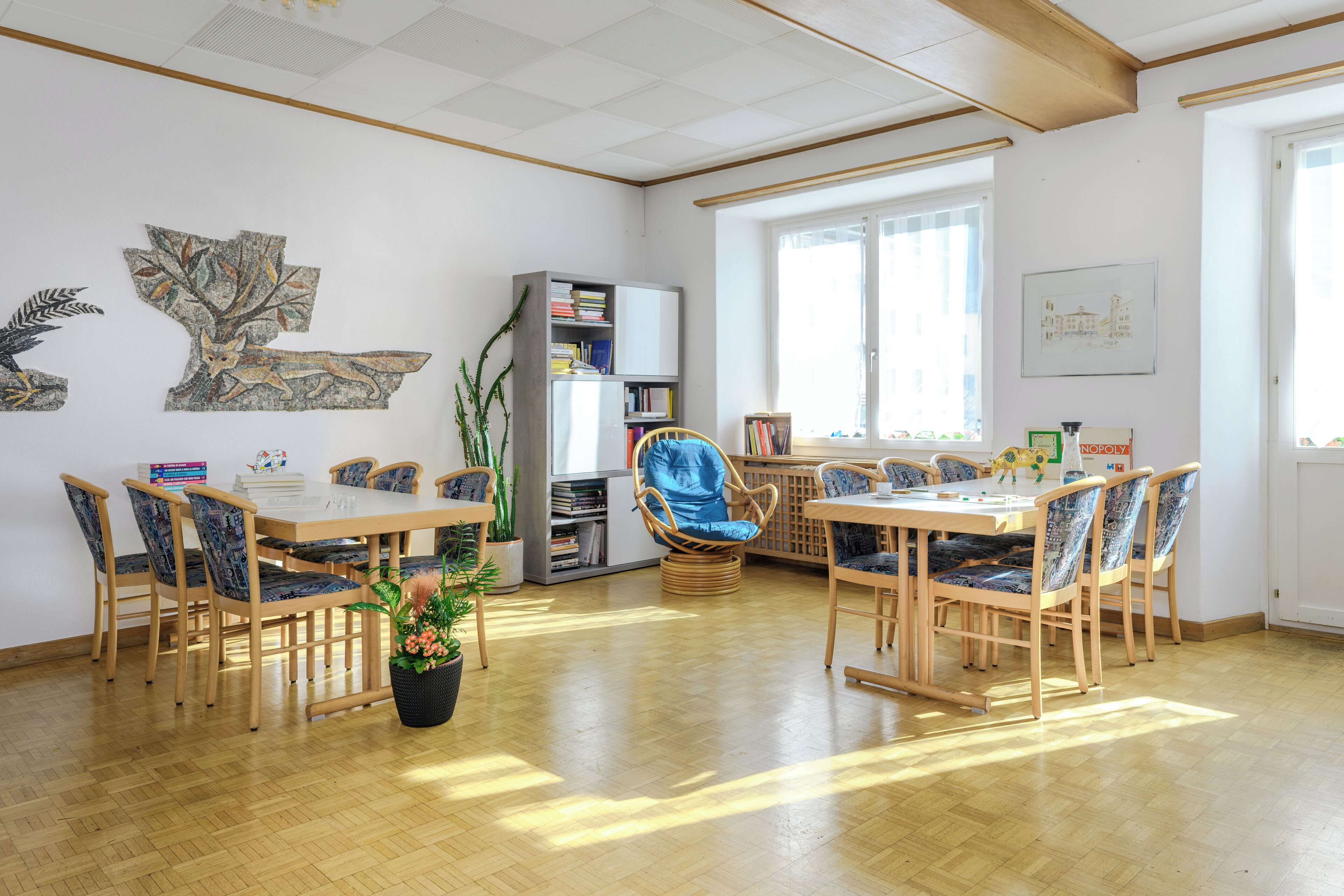 Una habitación con piso de madera, una mesa de comedor con sillas, una estantería y una ventana.