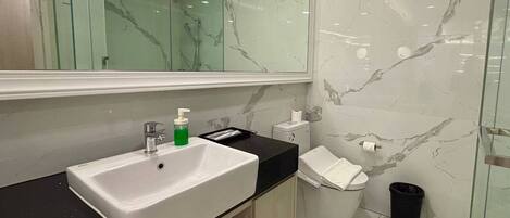 A modern bathroom with a white sink, a mirror, a toilet, and a trash bin.
