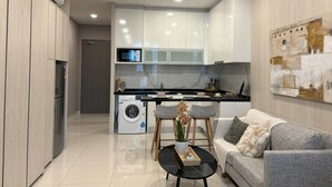 Une cuisine moderne avec des meubles blancs, un four à micro-ondes encastré et un lave-linge. On y trouve un canapé gris avec un coussin et une table basse noire avec un plateau.
