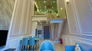 Un vaste espace de vie agrémenté d’un lustre moderne, d’un escalier et d’un coin salon avec des meubles aux motifs bleus.