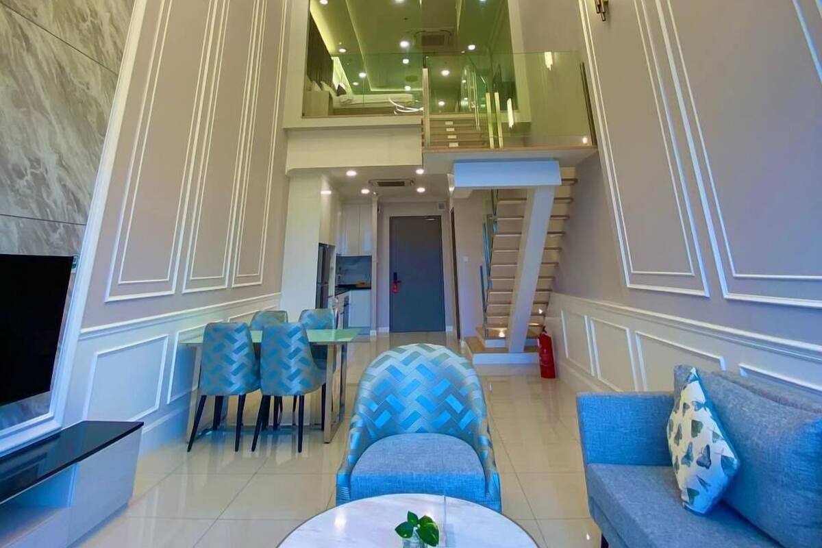 A spacious living area with a modern chandelier, a staircase, and a seating area with blue patterned furniture.