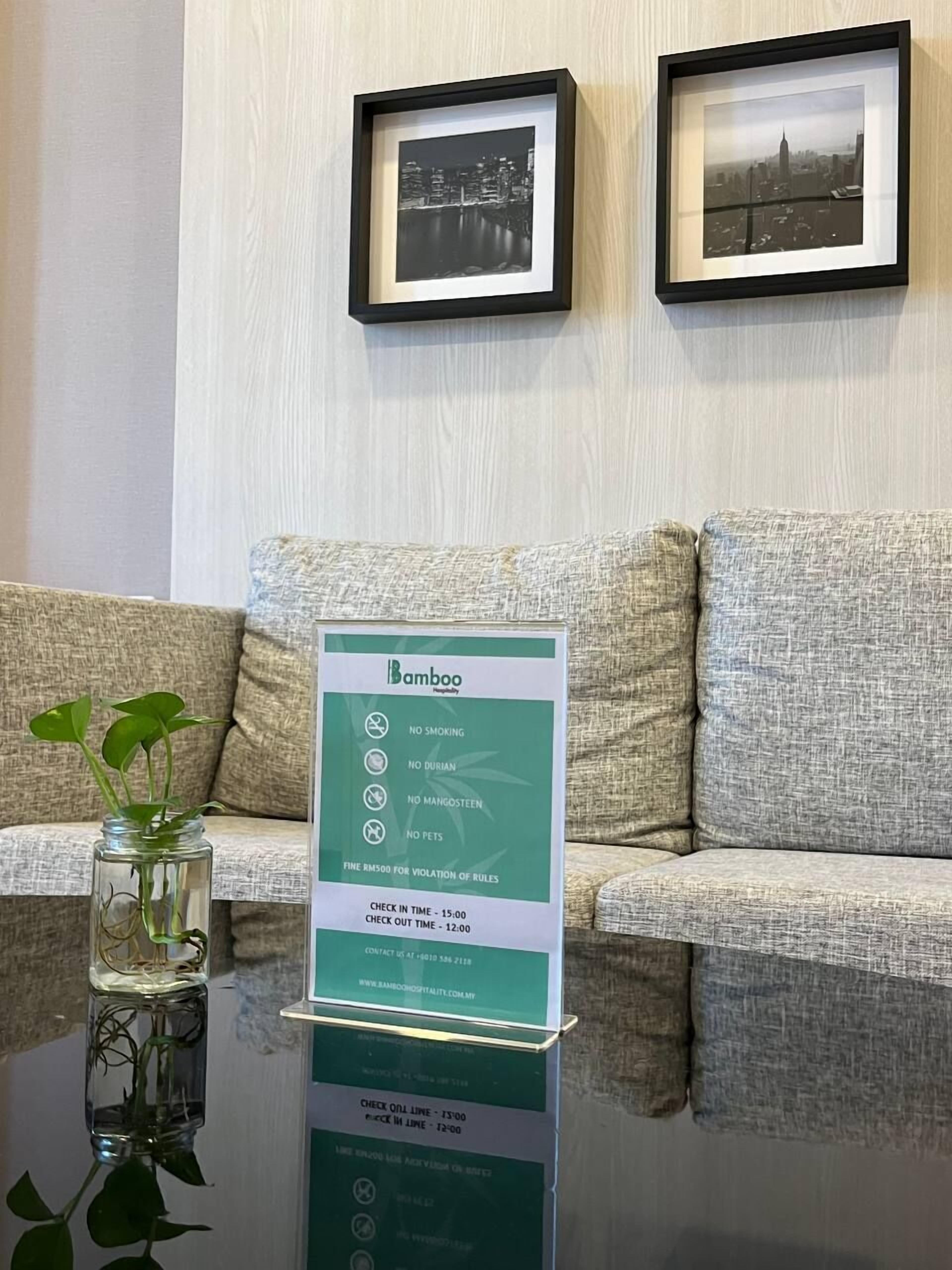 A framed cityscape picture, a framed Bamboo sign with rules, and a glass vase with a plant on a table.