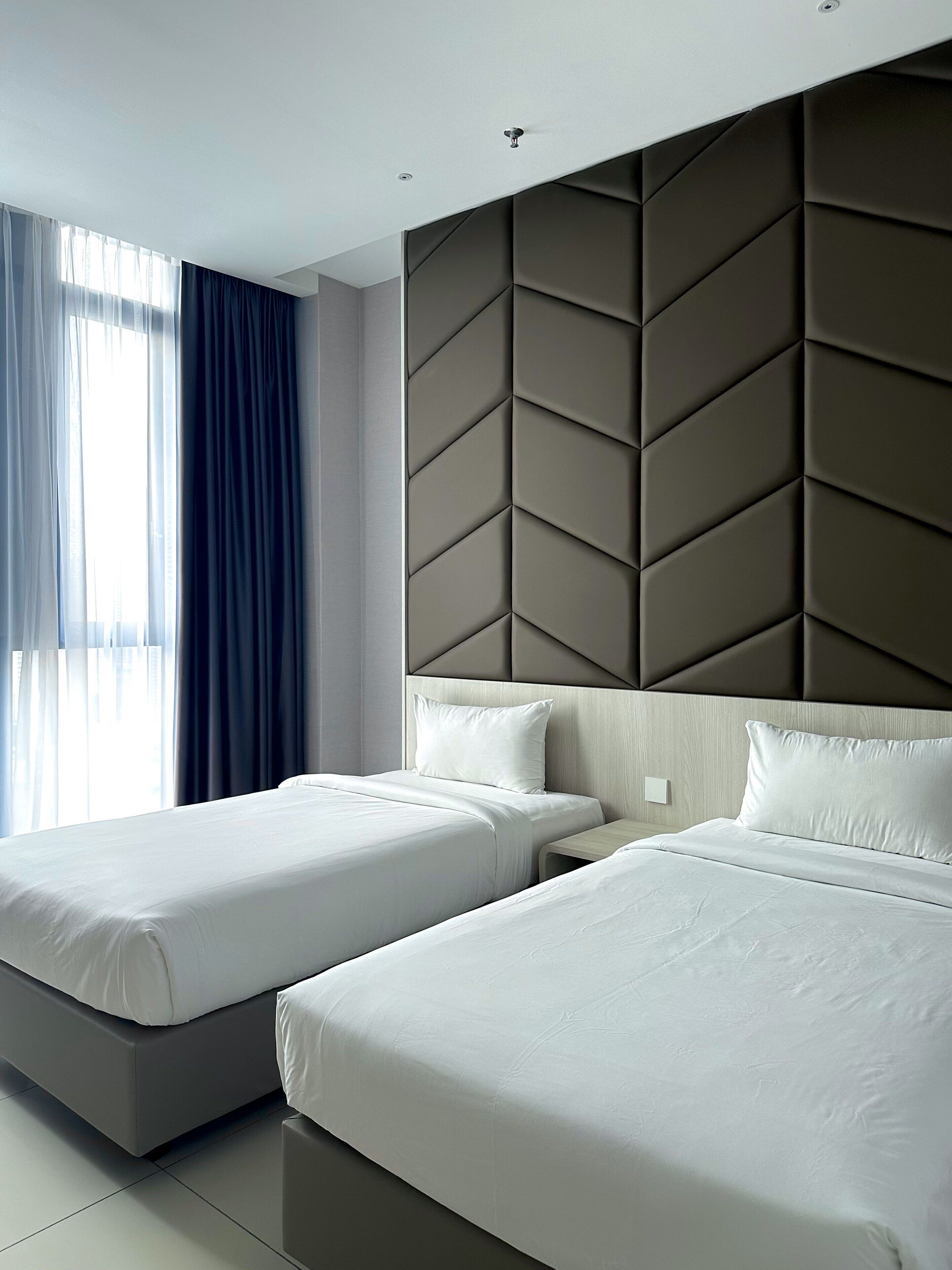 A hotel room with two beds, a modern headboard, and a large window with curtains.