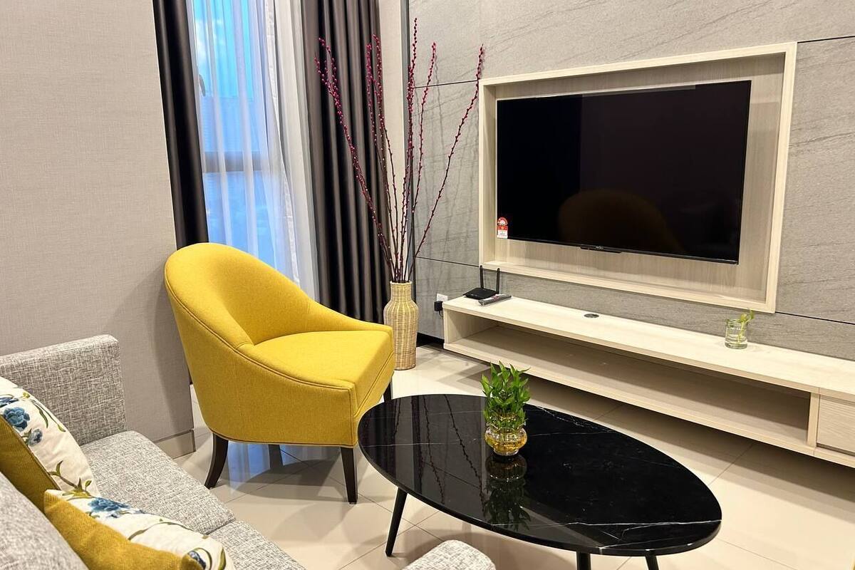 A modern living room with a yellow armchair, a black coffee table, and a flat-screen TV mounted on a light-colored wall.