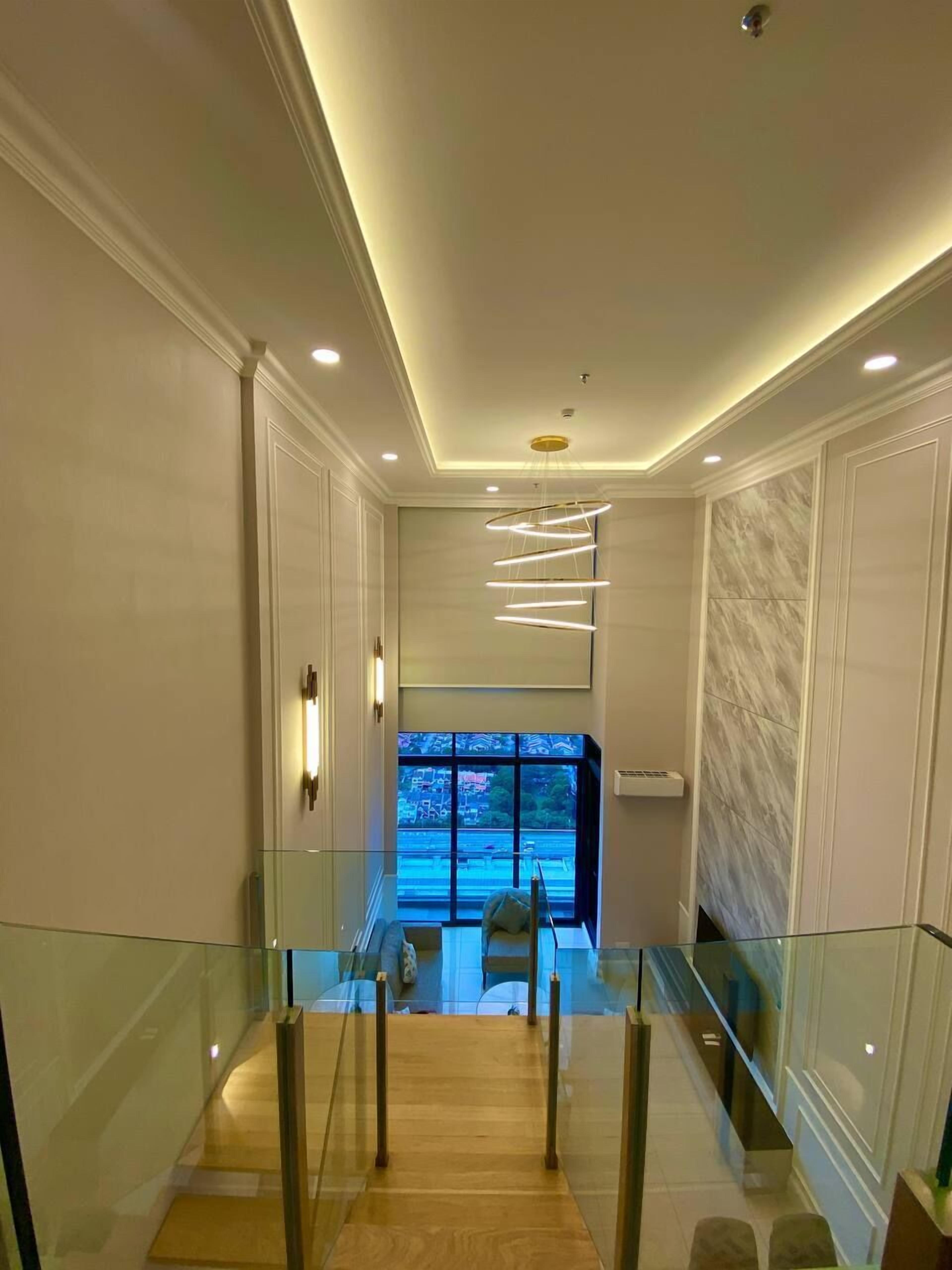 Un interior moderno con barandilla de vidrio, escalera de madera y vista a través de un amplio ventanal.