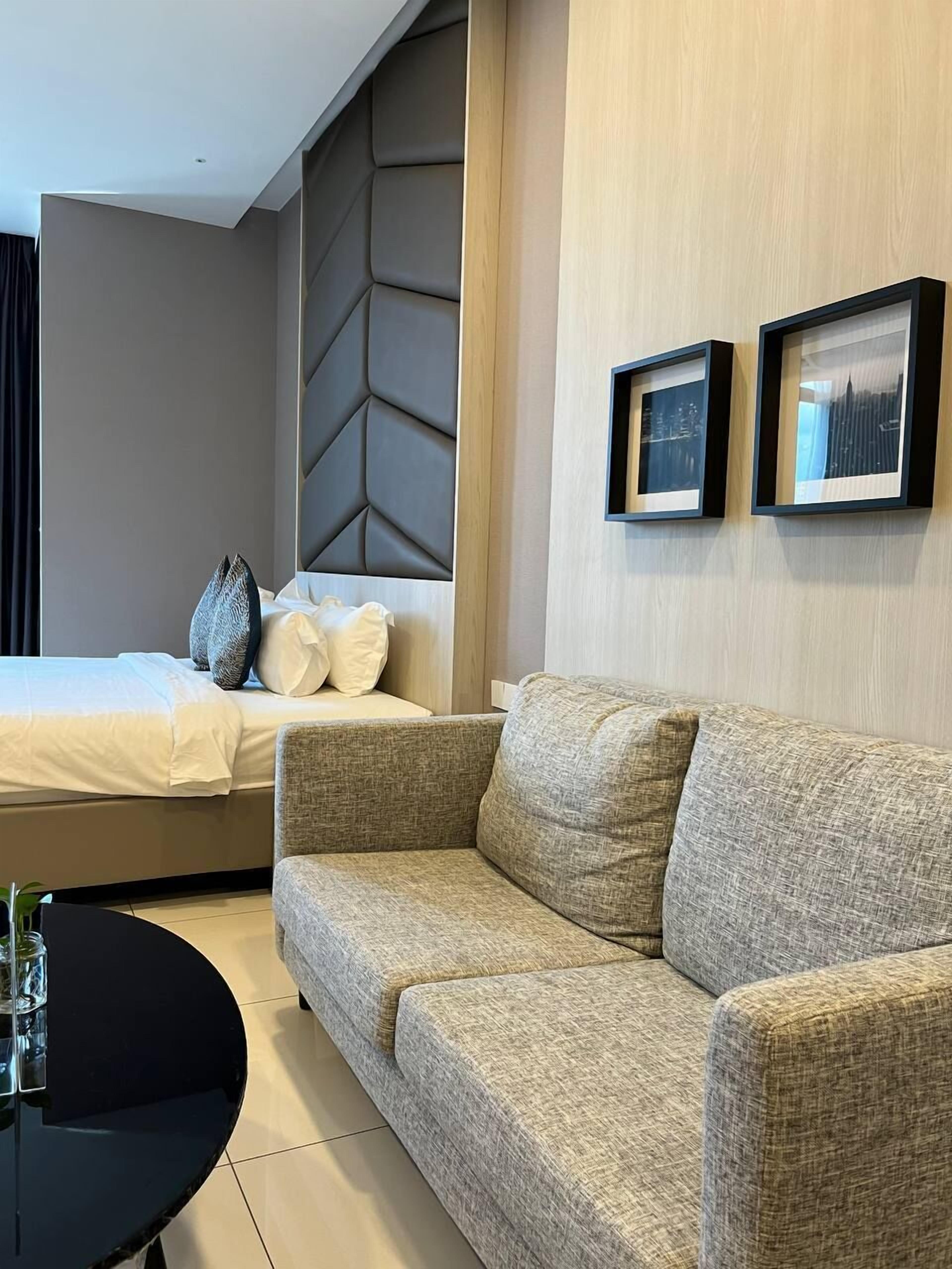 Une chambre d’hôtel moderne avec un lit, un canapé, une table ronde noire et deux tableaux encadrés accrochés au mur.