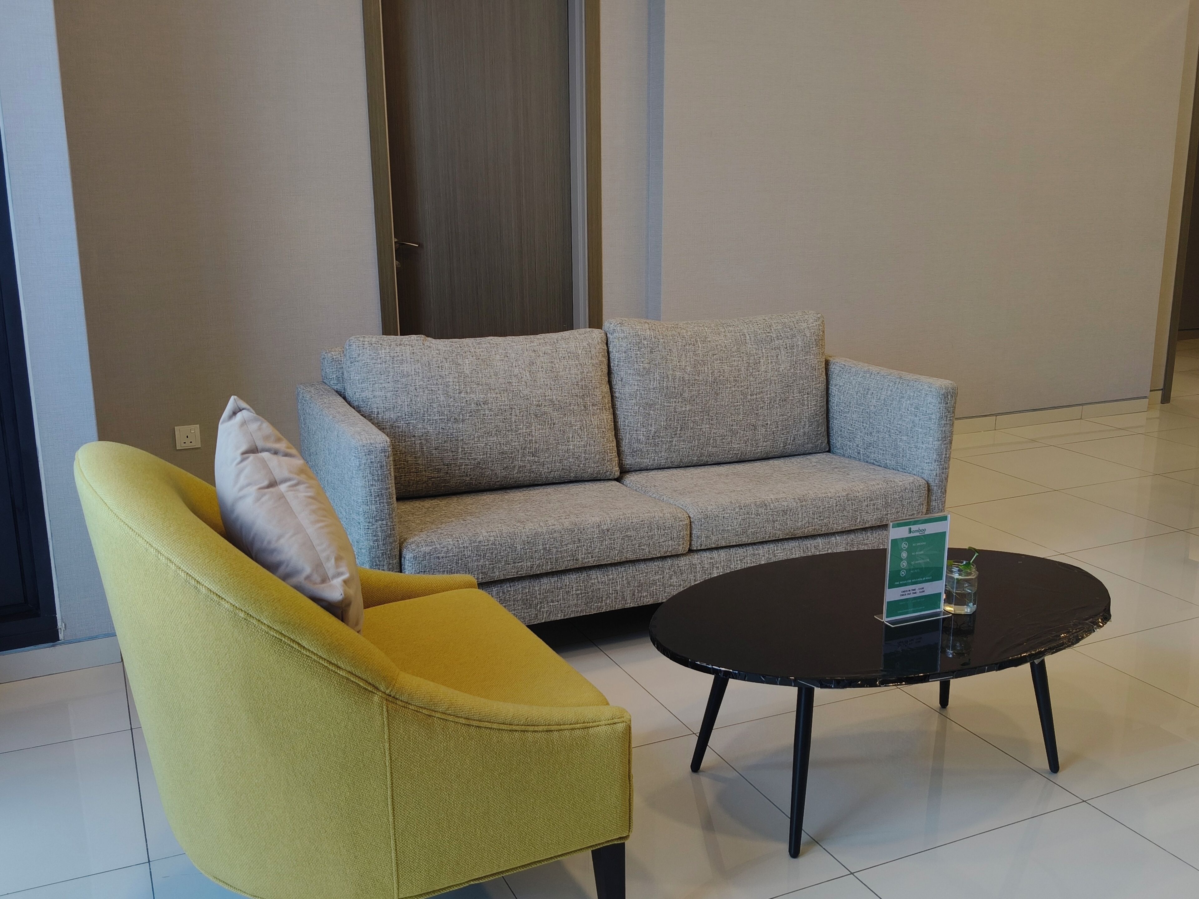 Een moderne woonkamer met een bank en fauteuil, een salontafel en een deur op de achtergrond.