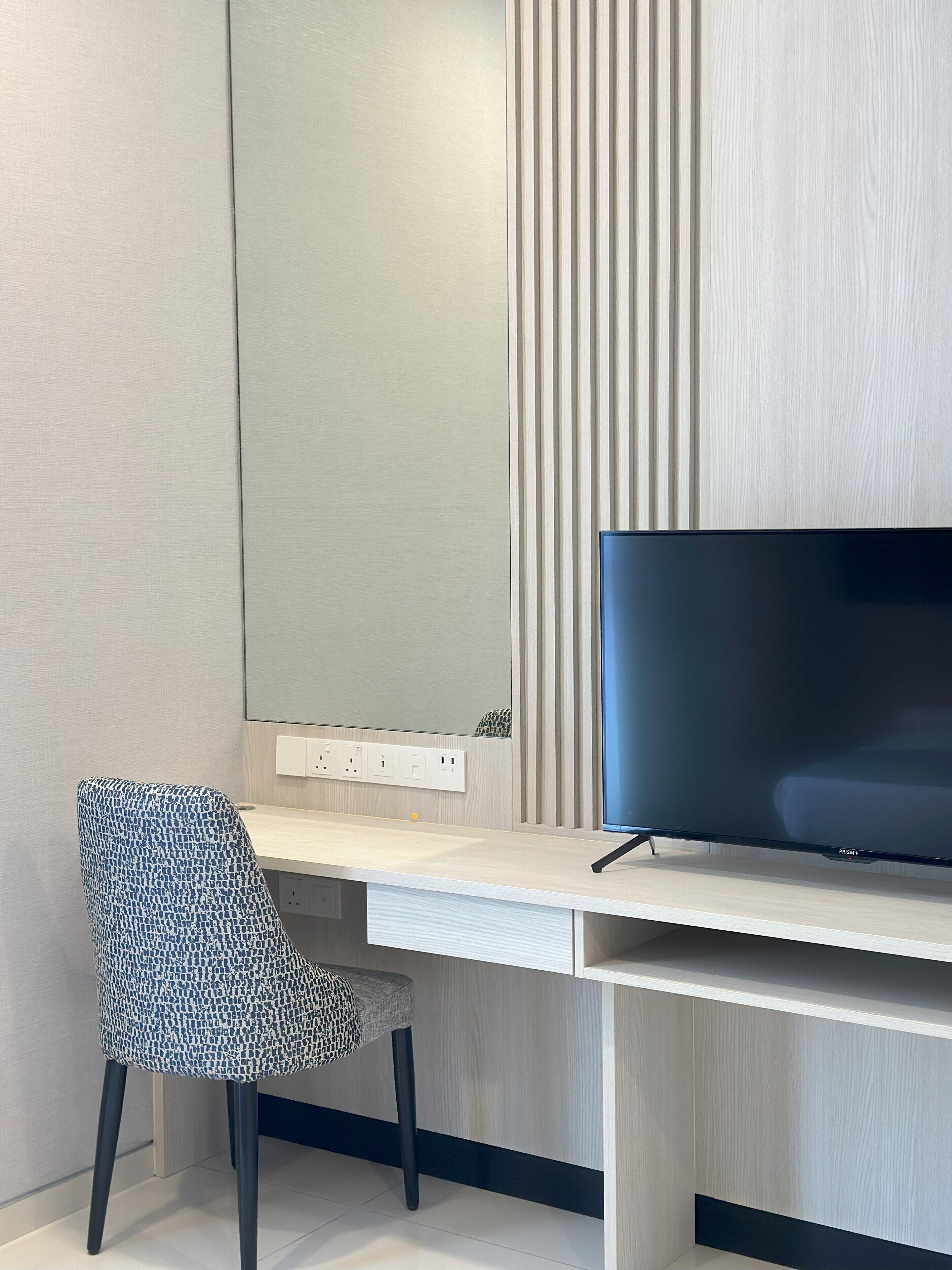 Una habitación moderna con un escritorio de madera, un televisor de pantalla plana y una silla estampada.