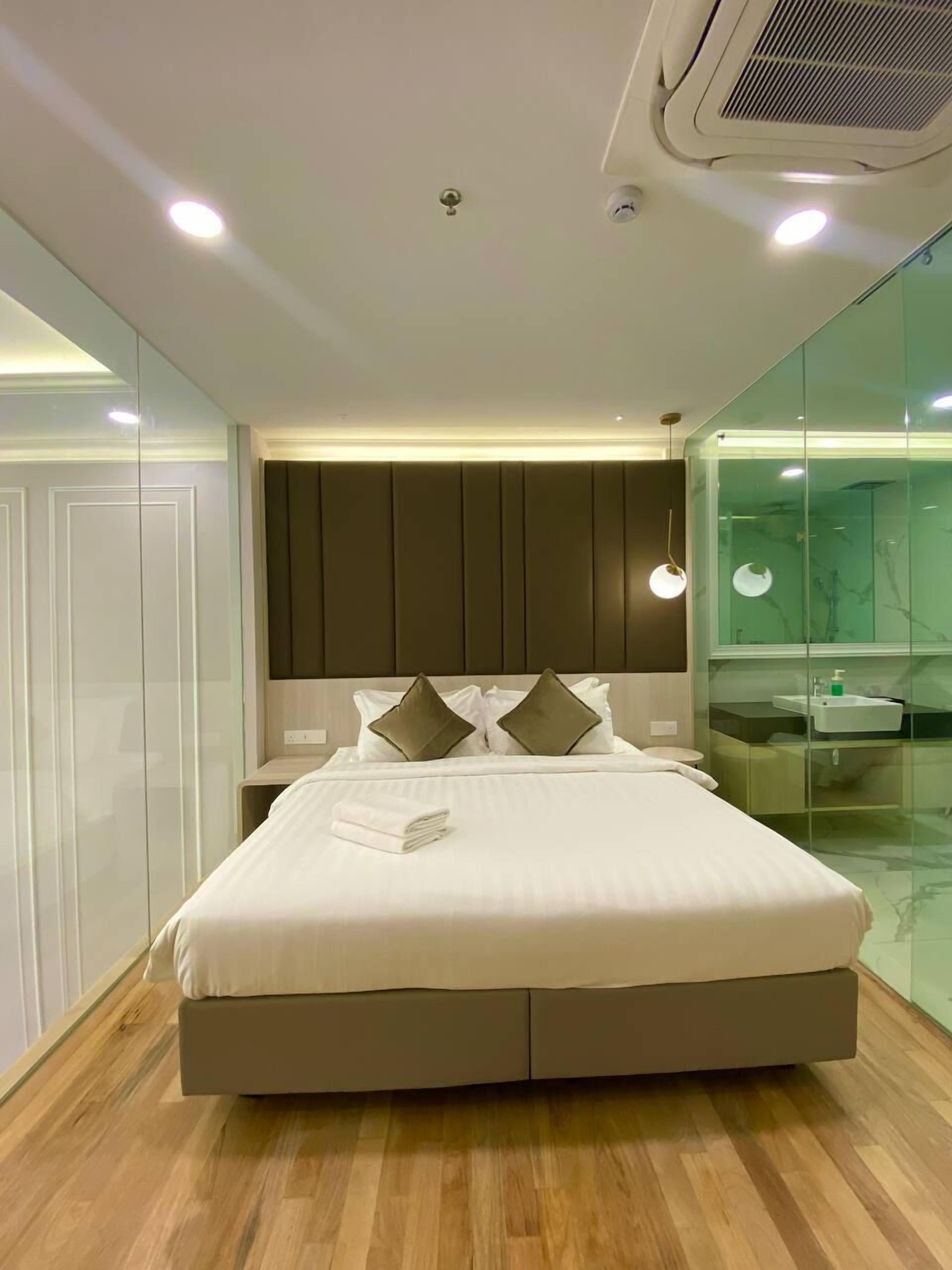 Un dormitorio moderno con una cama grande, separador de vidrio, tocador empotrado e iluminación empotrada en el techo.