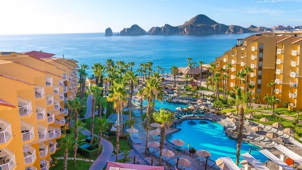 A resort with a pool, palm trees, and a view of the sea.