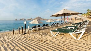 A beach with rows of sun loungers and umbrellas, a clear view of the sea, and rocky formations in the background.