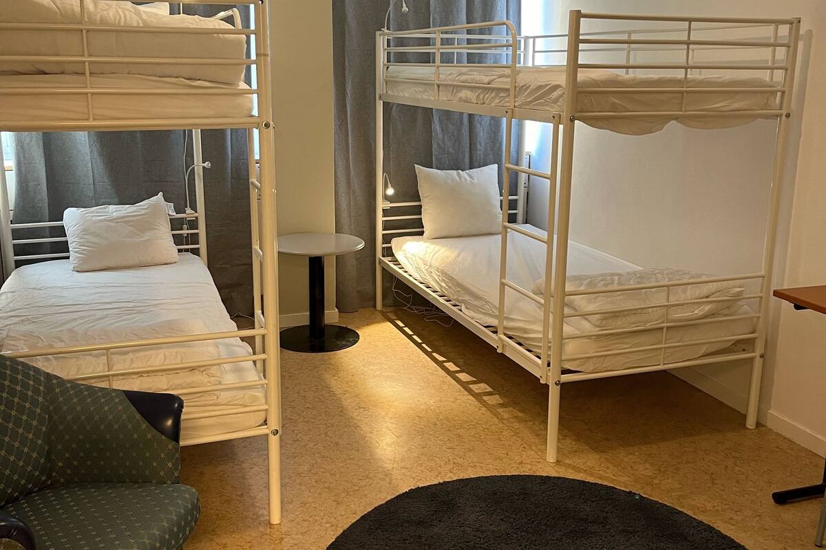A room with bunk beds, a small table, and a green armchair.