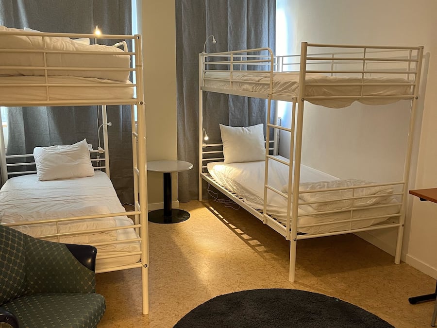 Ein Zimmer mit Etagenbetten, einem kleinen Tisch und einem grünen Sessel.