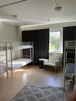 A dormitory room with bunk beds, a small round table, a chair, and a window with curtains. - City Hostel 46 (Örebro)