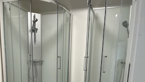 Zona de ducha con paredes de vidrio y diseño curvo, cabezal de ducha de mano y grifo empotrado en la pared.