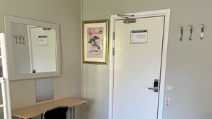 Una habitación pequeña y limpia, con escritorio, silla y una puerta con un cartel.
