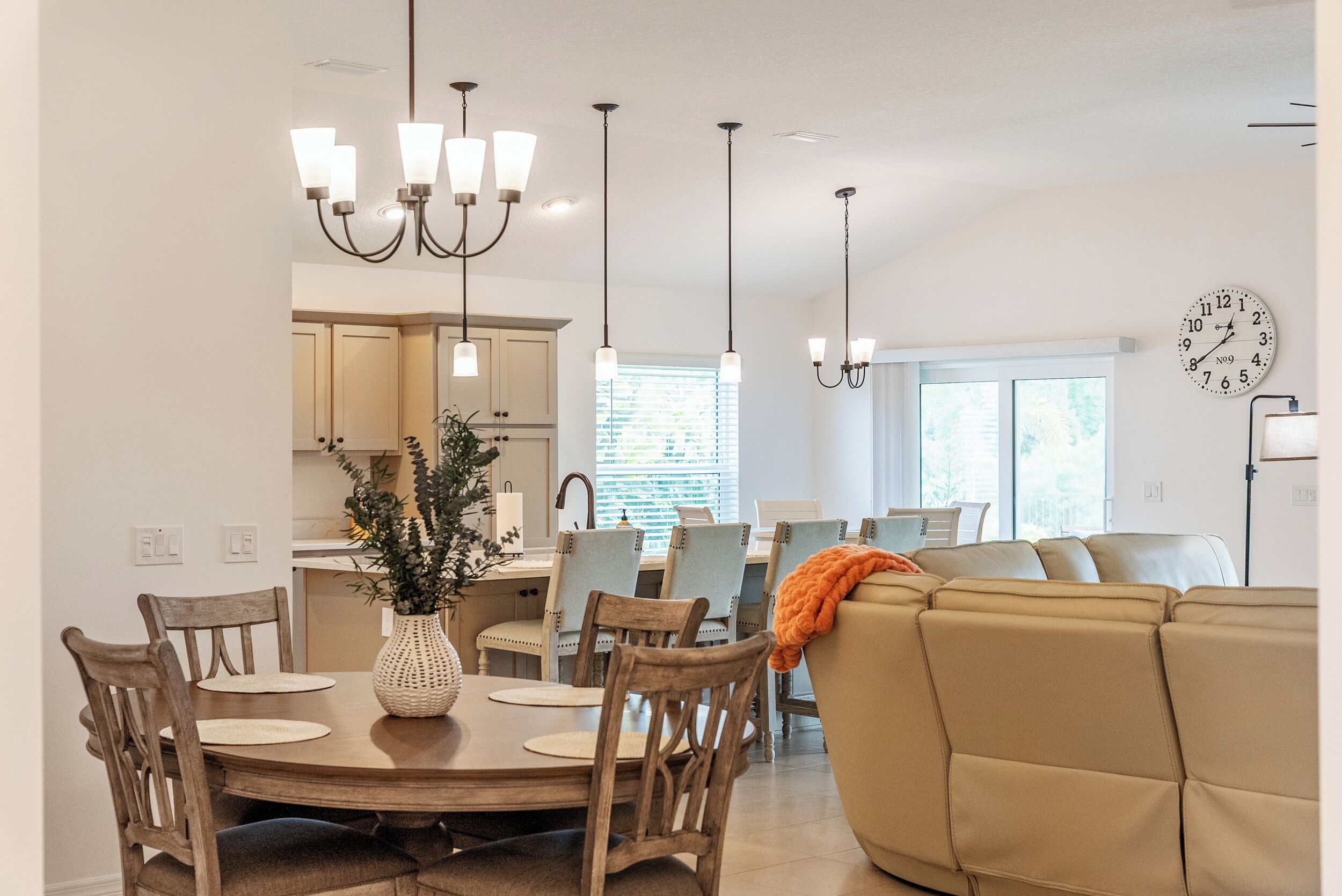 A modern kitchen with pendant lighting, a dining table with chairs, and a living area with a sofa.