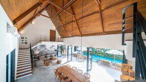 A spacious living area with a wooden ceiling, a dining table, and a staircase. - Villa Nusantara 5 by Alfred in Bali - Promo Luxury 4BD Pool Villa Pererenan Beach Caggu (Canggu)