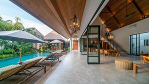A modern indoor pool area with lounge chairs, a wooden ceiling, and a staircase leading to a dining area. - Villa Nusantara 5 by Alfred in Bali - Promo Luxury 4BD Pool Villa Pererenan Beach Caggu (Canggu)