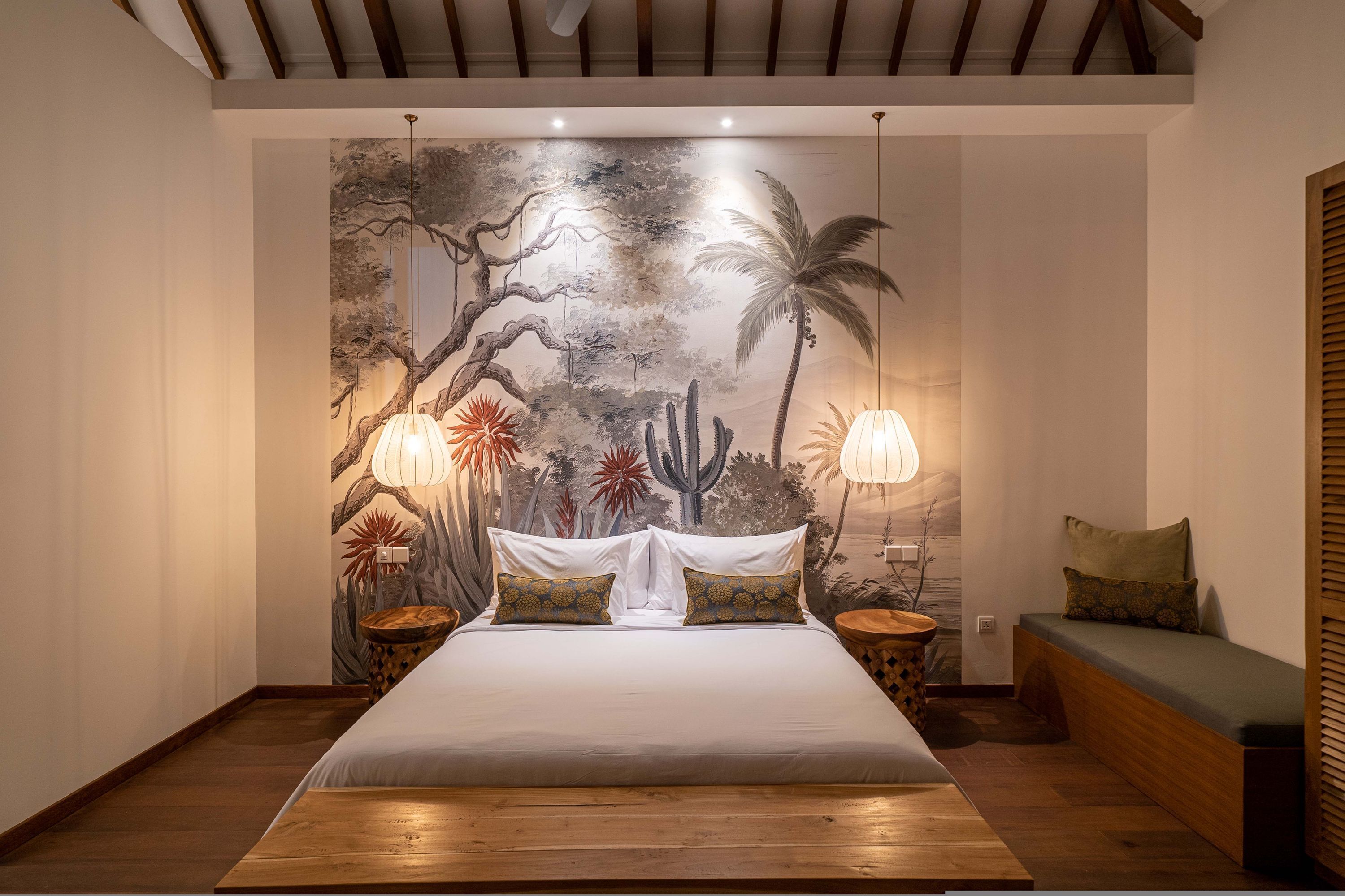A bedroom with a large bed, two bedside tables, a wooden bench, and a mural on the wall.