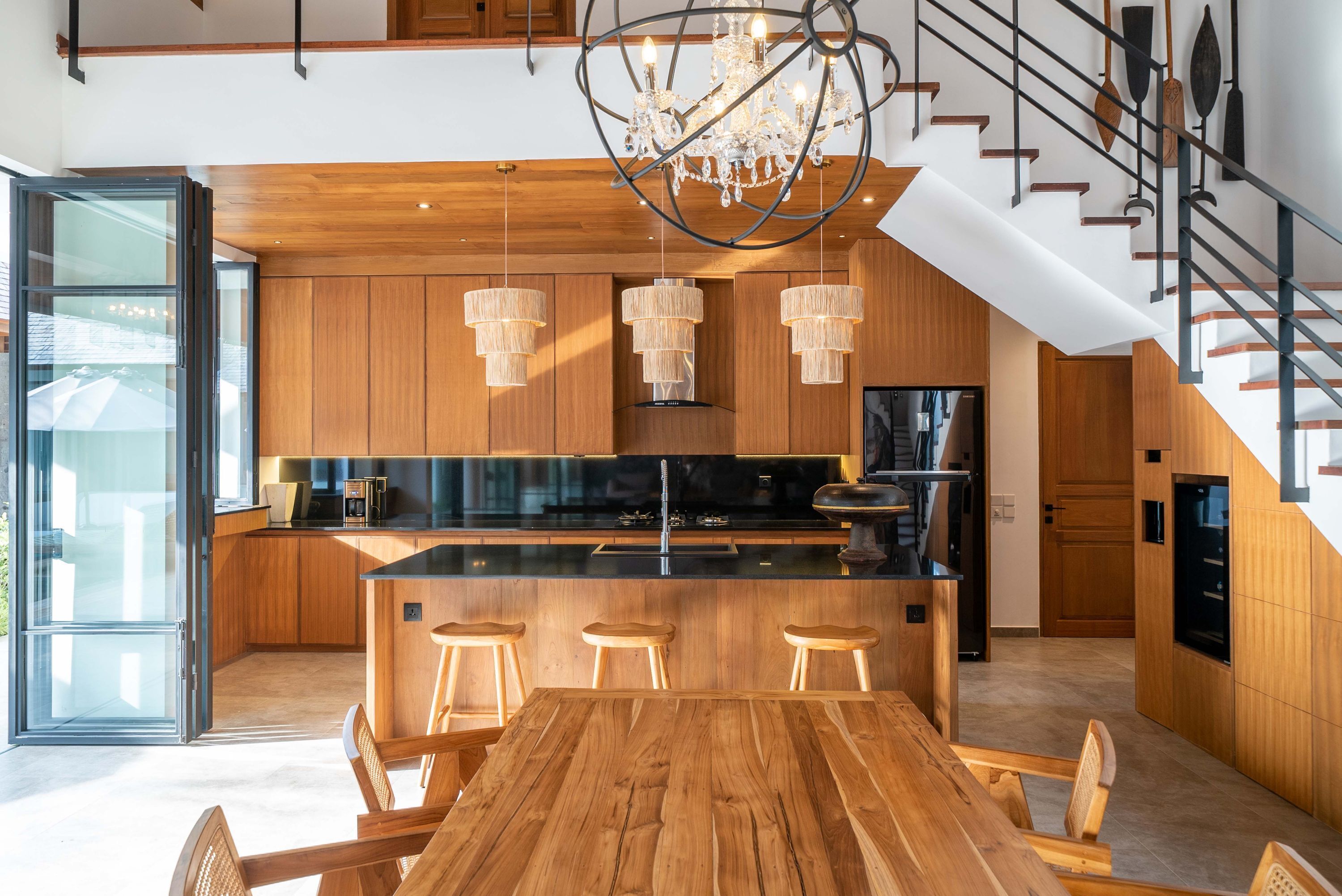 Een moderne keuken met houten kastjes, een centraal eiland met krukken, en een kroonluchter.