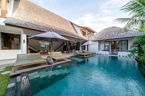 A modern house with a swimming pool, lounge chairs, and umbrellas.