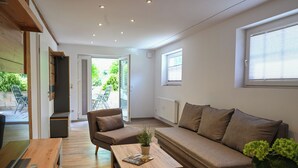 A modern living room with a sofa, a coffee table, and a TV. There is a sliding door leading to an outdoor area with a table and chairs. - Romantic mill arbor "At the foot of the Staffelberg" (Bad Staffelstein)